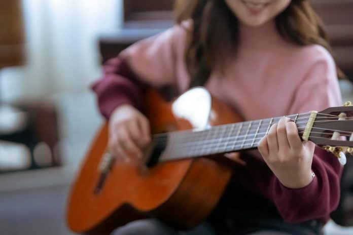crop woman playing guitar near piano